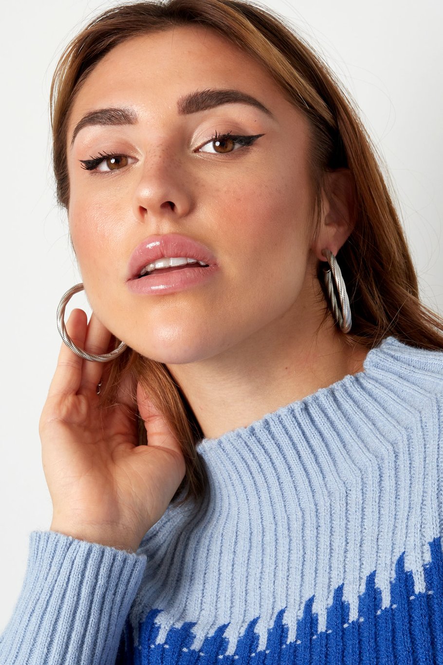 Mujer con jersey azul claro luciendo pendientes de aro plateado
