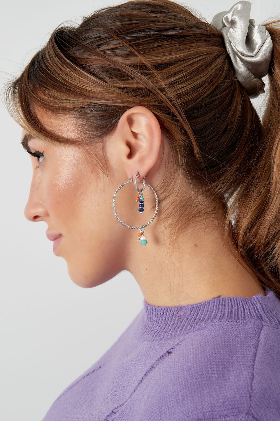 Modelo con pendientes plateados con charms coloridos en forma de aro grande.