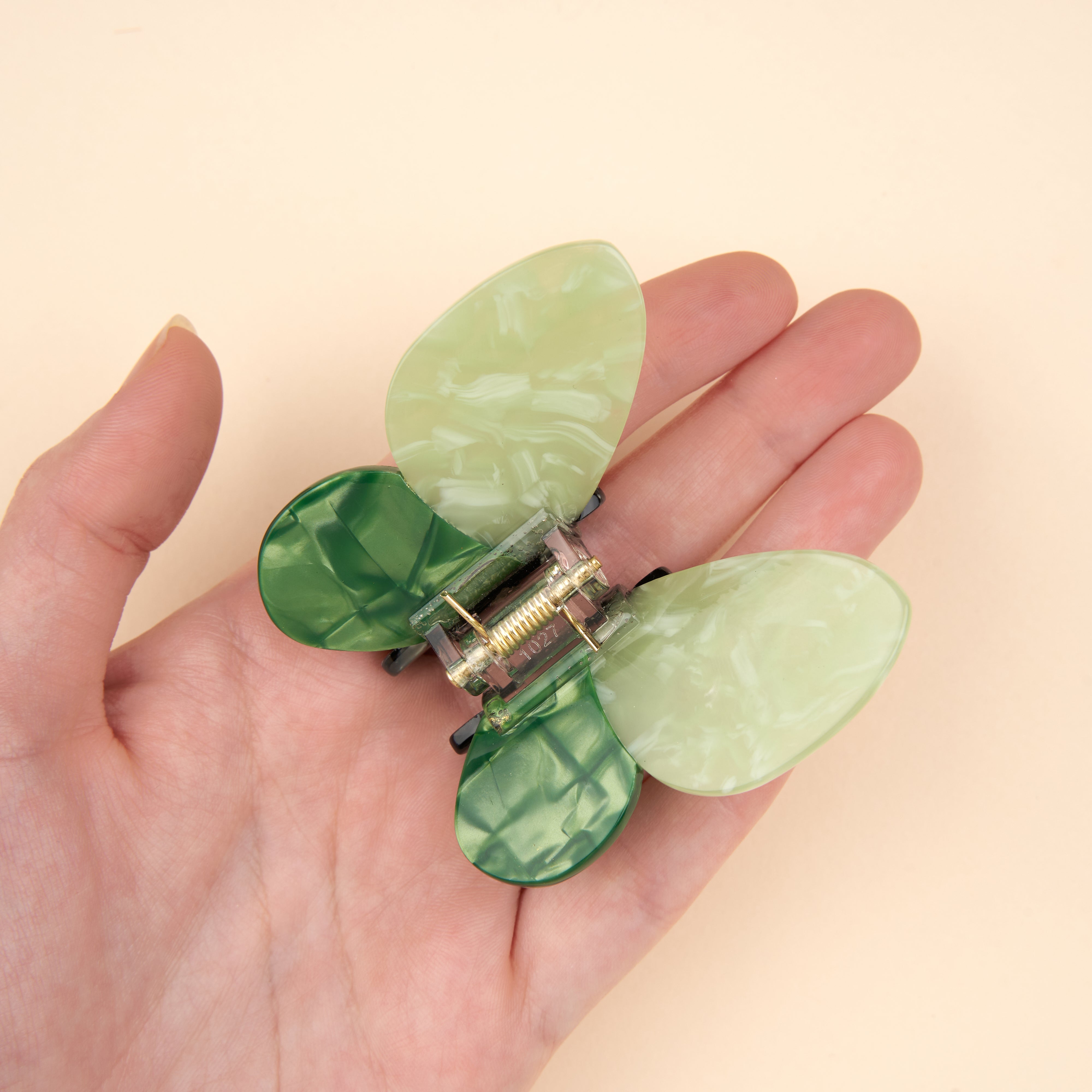 Pinza de pelo con forma de mariposa verde, sostenida en la mano