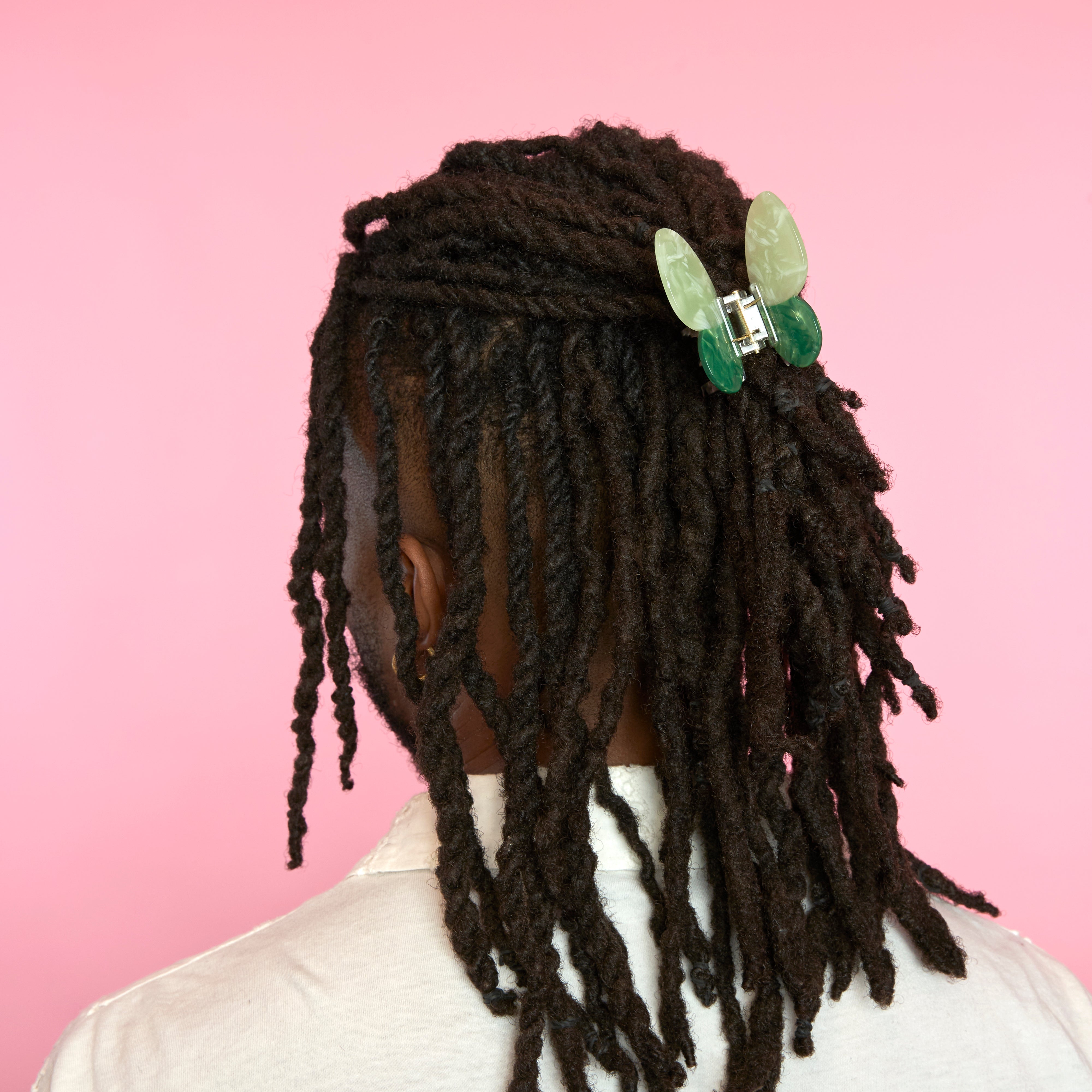 Persona con trenzas recogidas usando pinza mariposa verde en el cabello