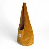Bolsa ovalada de pana color mostaza, vista lateral mostrando su forma.
