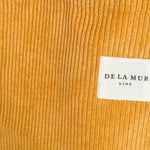 Detalle del tejido de pana mostaza con etiqueta frontal de la marca De La Mur.
