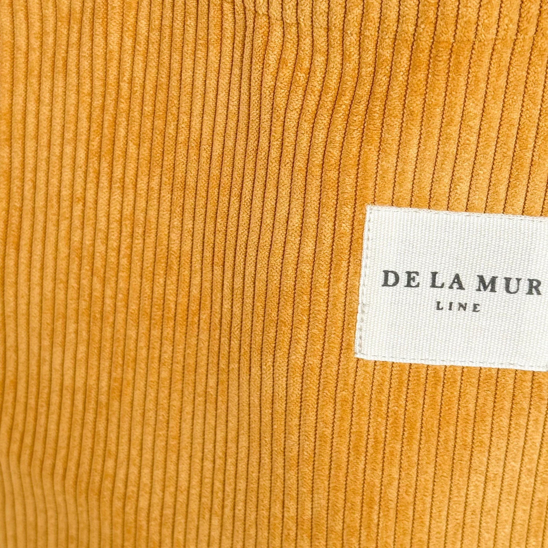 Detalle del tejido de pana mostaza con etiqueta frontal de la marca De La Mur.