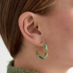 Aros dorados con cuentas verdes y turquesas en espiral, vista frontal sobre fondo blanco.