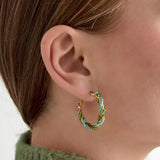 Aros dorados con cuentas verdes y turquesas en espiral, vista frontal sobre fondo blanco.