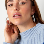 Mujer con jersey azul claro luciendo pendientes de aro plateado

