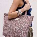 Bolsa shopper grande de jacquard con estampado geométrico en tonos lila y rosa llevada al hombro.