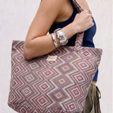 Bolsa shopper grande de jacquard con estampado geométrico en tonos lila y rosa llevada al hombro.