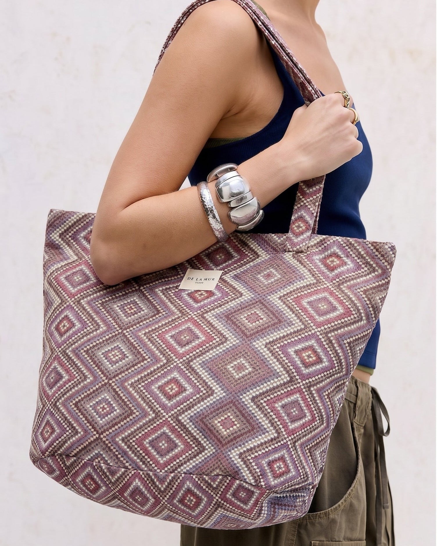 Bolsa shopper grande de jacquard con estampado geométrico en tonos lila y rosa llevada al hombro.