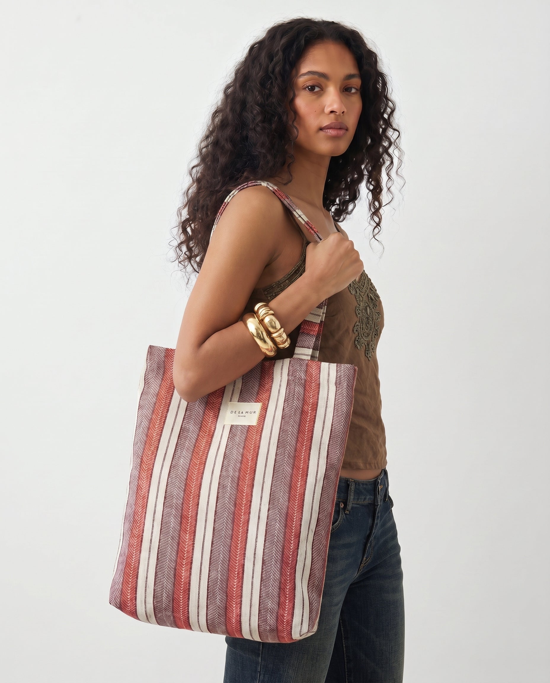 Mujer llevando una bolsa tote de jacquard con estampado de rayas en tonos rojo, granate, lila y crudo.