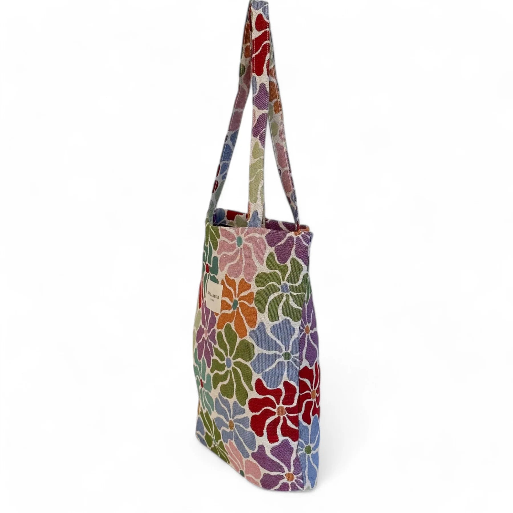 Vista lateral de tote bag floral con asas largas, fondo blanco.