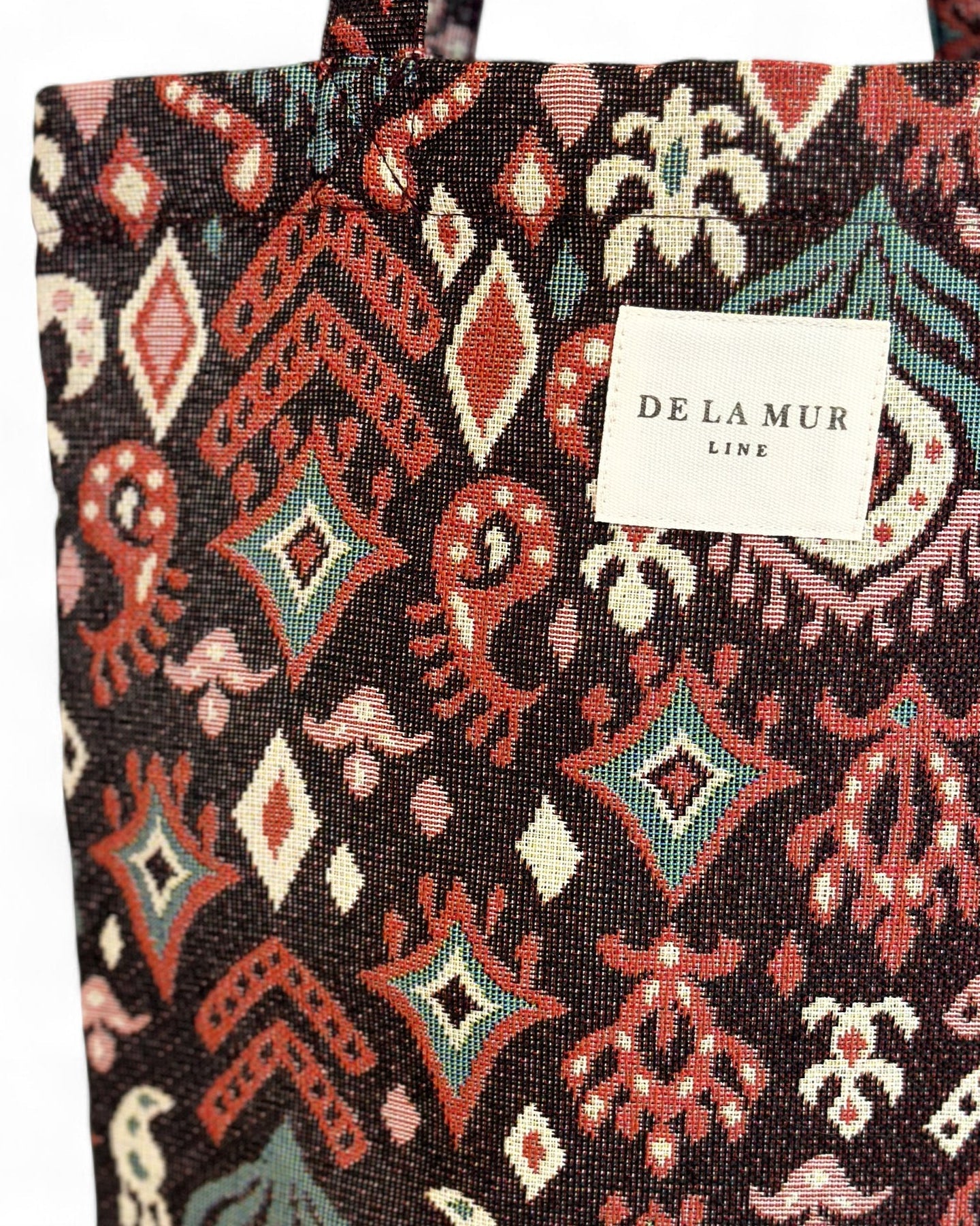 Detalle de tejido grueso jacquard con motivos granates y etiqueta De La Mur