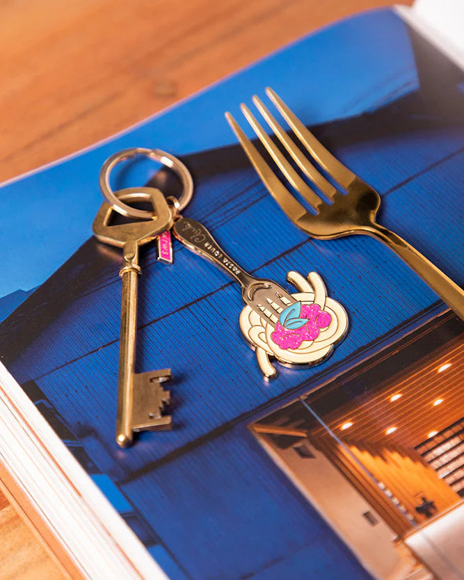 Llavero esmaltado dorado con diseño de tenedor y plato de pasta.