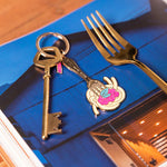 Llavero esmaltado dorado con diseño de tenedor y plato de pasta.