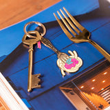 Llavero esmaltado dorado con diseño de tenedor y plato de pasta.