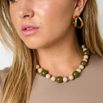 Collar de cuentas acrílicas verdes y beige con detalles de acero colocado sobre una modelo.