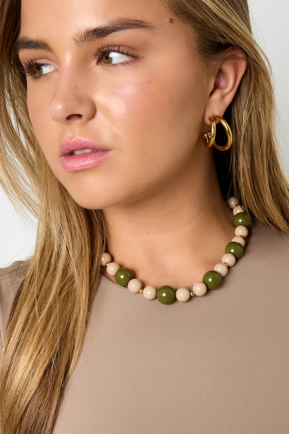 Collar de cuentas acrílicas verdes y beige con detalles de acero colocado sobre una modelo.