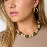 Collar de cuentas acrílicas verdes y beige con detalles de acero colocado sobre una modelo.