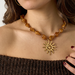 Mujer con collar de cuentas ámbar y colgante de sol dorado de acero inoxidable.