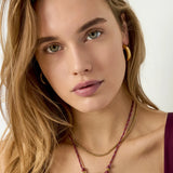 Collar con colgante de sol dorado y cordón burdeos colocado sobre una modelo.