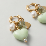 Detalle de pendientes con corazón verde de cerámica, perla y pequeños cristales.