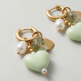 Detalle de pendientes con corazón verde de cerámica, perla y pequeños cristales.