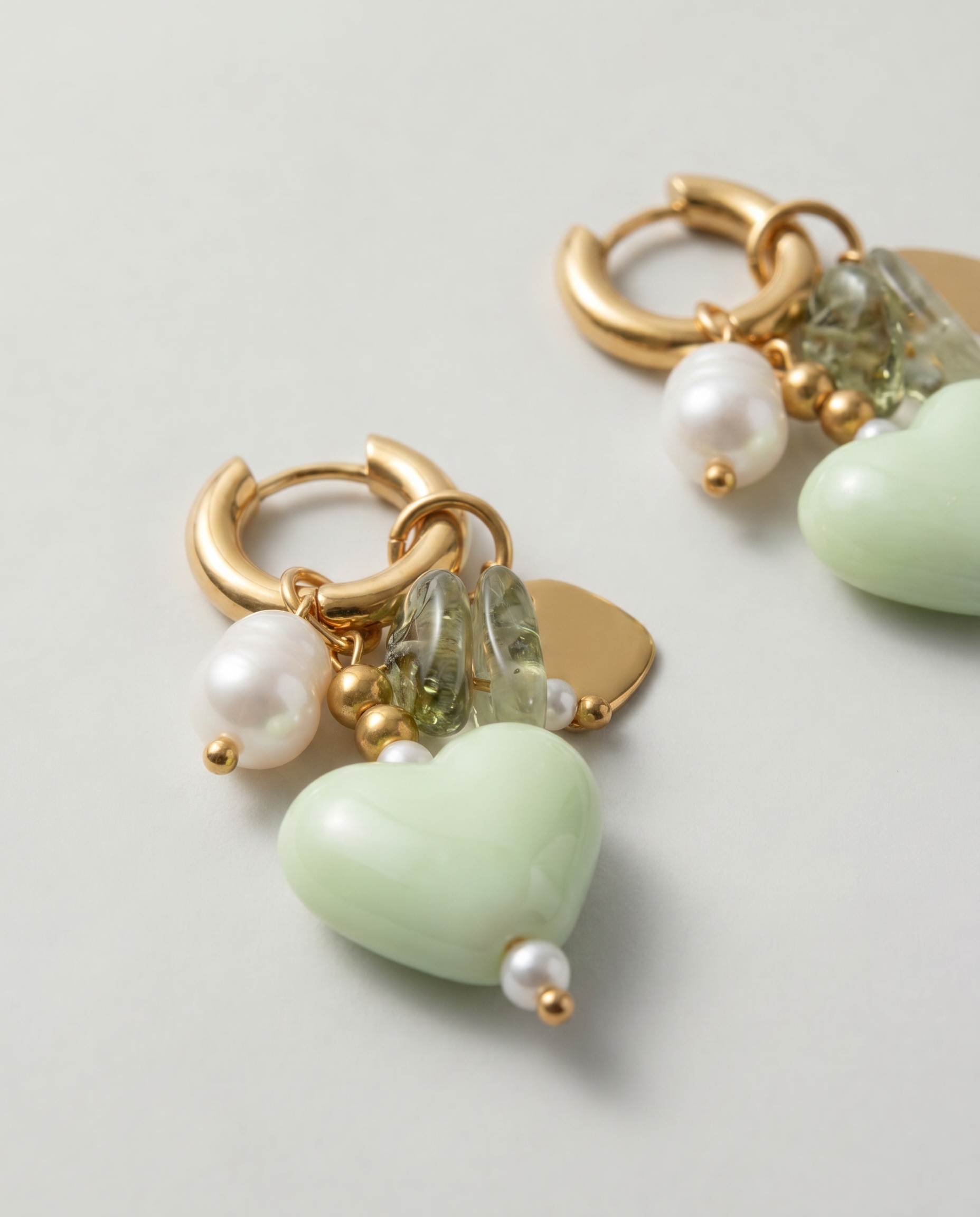 Detalle de pendientes con corazón verde de cerámica, perla y pequeños cristales.
