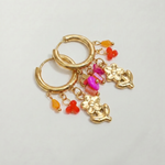 Detalle de pendientes de acero inoxidable con colgante de ángel y pequeños charms de colores.