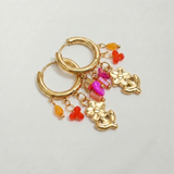 Detalle de pendientes de acero inoxidable con colgante de ángel y pequeños charms de colores.