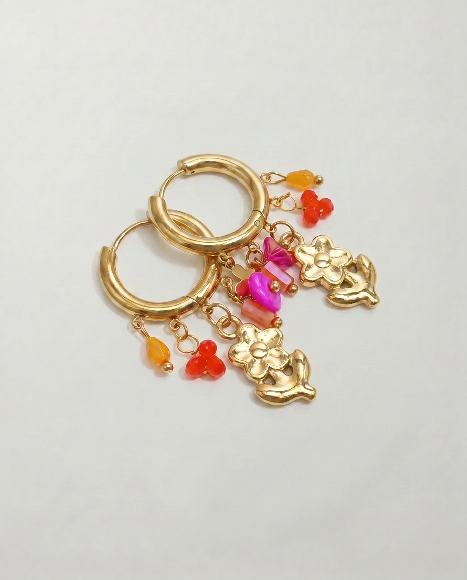 Detalle de pendientes de acero inoxidable con colgante de ángel y pequeños charms de colores.