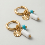 Detalle de pendientes de aro dorados con piedras blancas y turquesas.