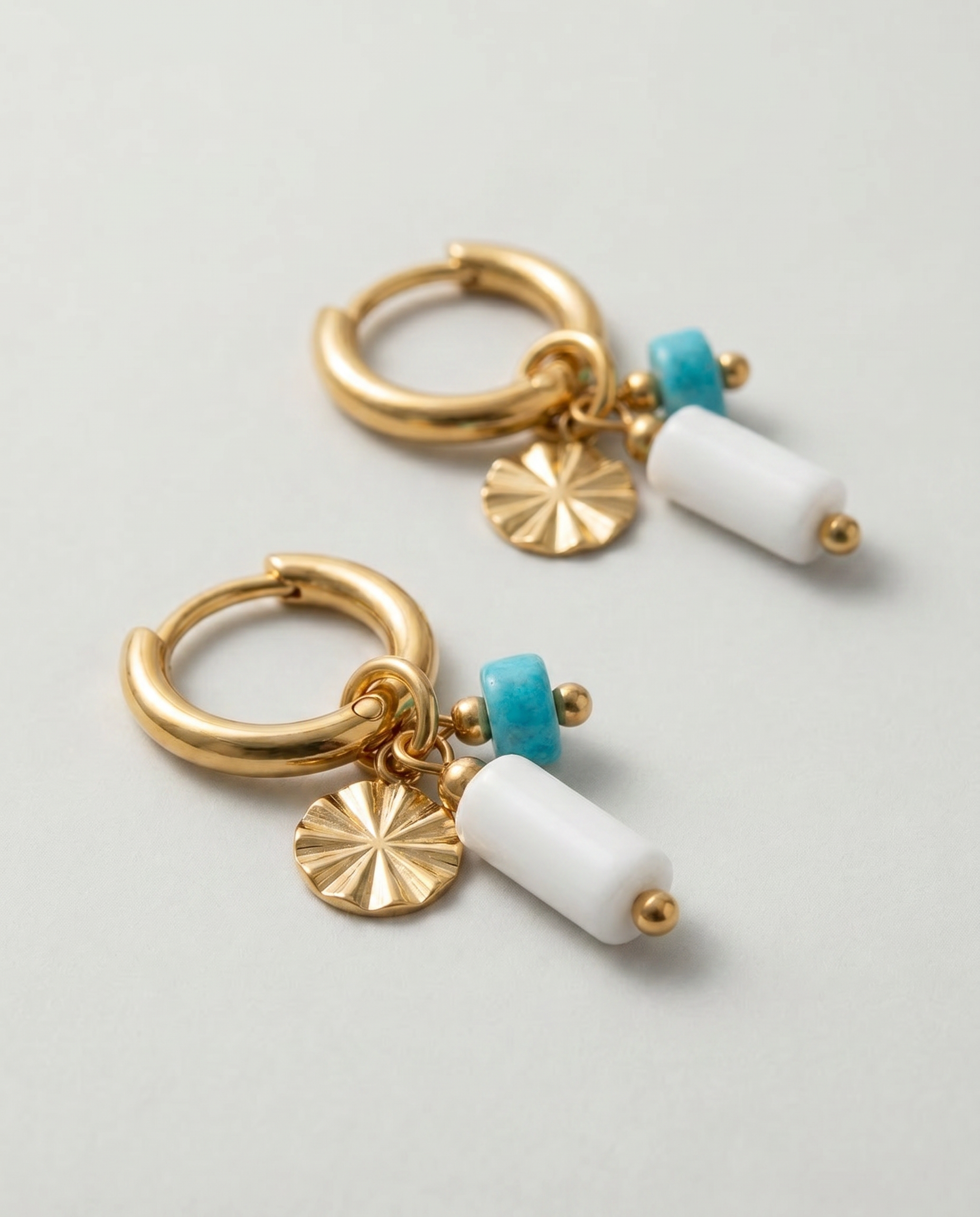 Detalle de pendientes de aro dorados con piedras blancas y turquesas.