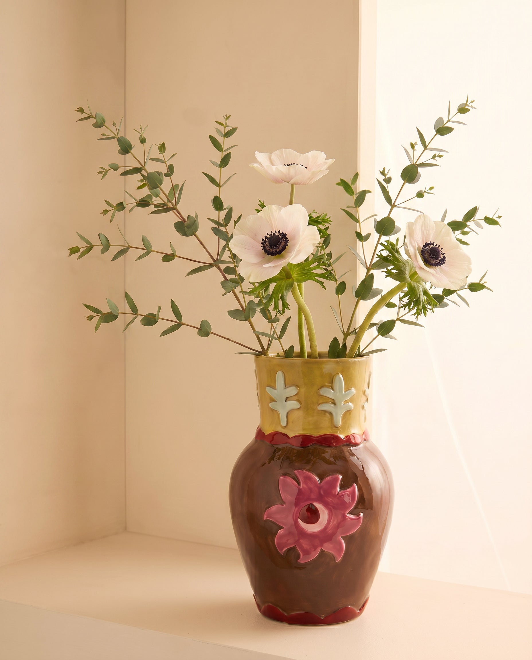 Jarrón de cerámica con flor rosa en relieve y flores blancas, vista frontal.