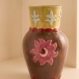 Jarrón de cerámica decorativo con flor rosa en relieve sobre fondo neutro.