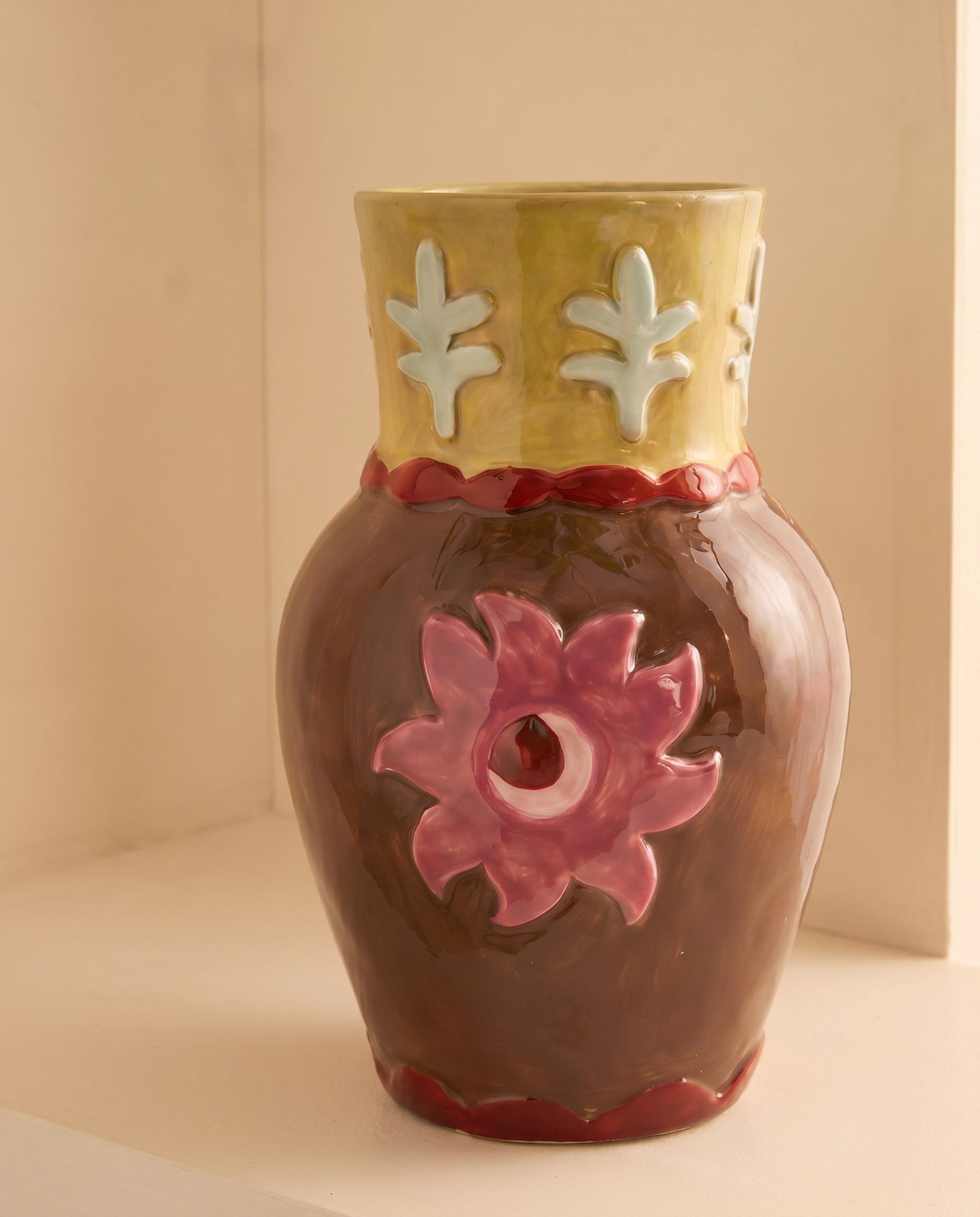 Jarrón de cerámica decorativo con flor rosa en relieve sobre fondo neutro.