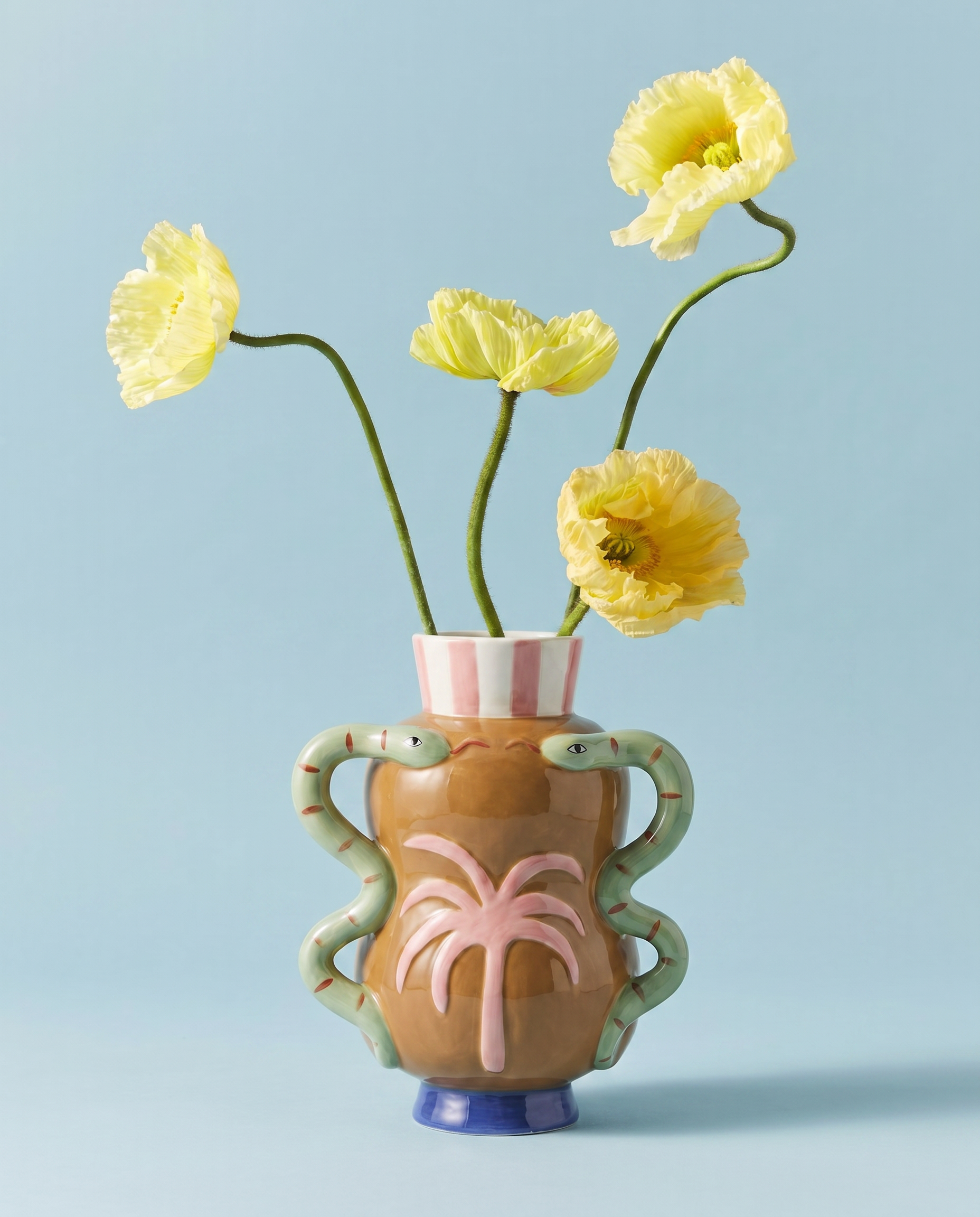 Jarrón de cerámica con palmera en relieve y serpientes, con flores amarillas.