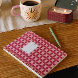 Libreta Pinwheel Pink sobre un escritorio junto a una taza de café y accesorios de papelería.