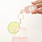 Llavero esmaltado con forma de botella de gin rosa con detalles dorados.