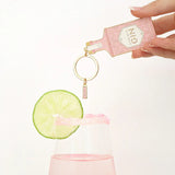 Llavero esmaltado con forma de botella de gin rosa con detalles dorados.
