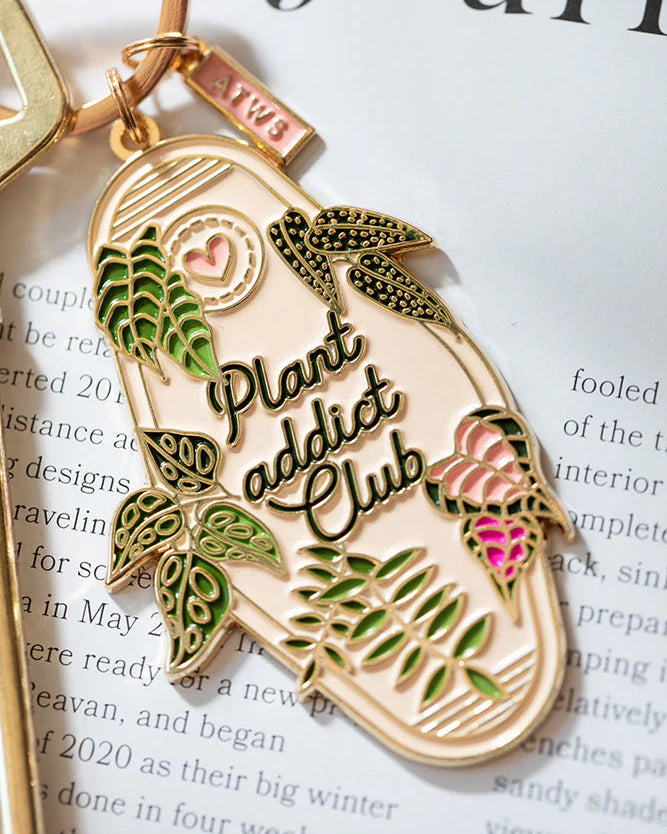 Detalle del llavero botánico con hojas verdes y rosas sobre fondo beige.