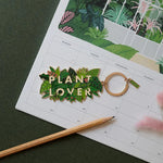 Llavero esmaltado con hojas verdes y letras Plant Lover en dorado.
