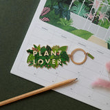 Llavero esmaltado con hojas verdes y letras Plant Lover en dorado.