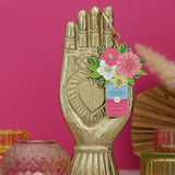 Detalle del llavero dorado con flores rosas y fondo rosa vibrante.