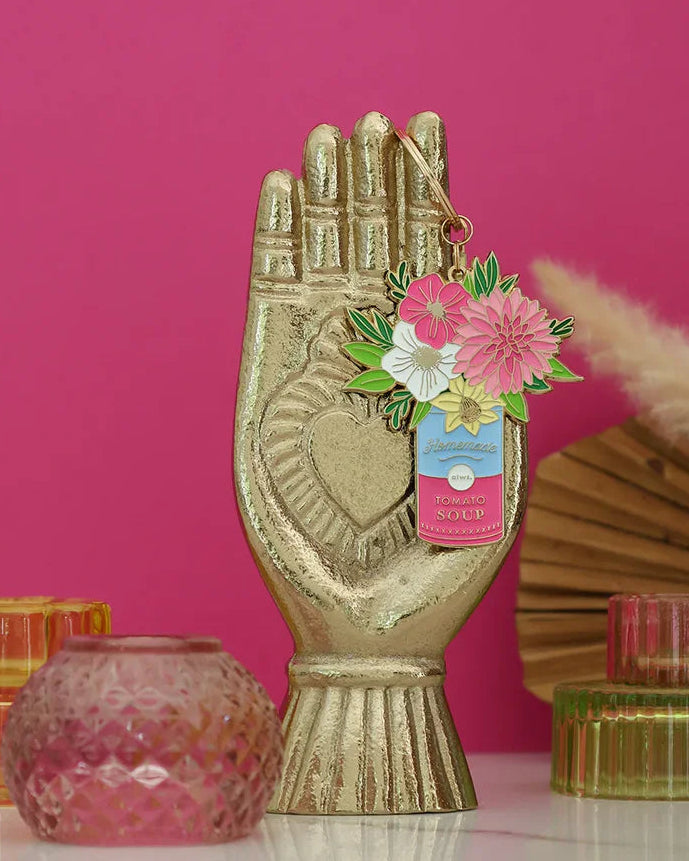 Detalle del llavero dorado con flores rosas y fondo rosa vibrante.