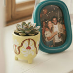 “Detalle del diseño floral rojo y blanco en la maceta de cerámica amarilla.