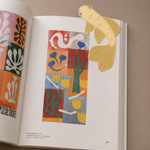 Marcapáginas de metal con diseño de pez koi marcando una página de un libro abierto.