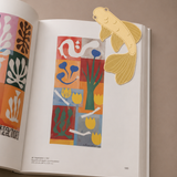 Marcapáginas de metal con diseño de pez koi marcando una página de un libro abierto.