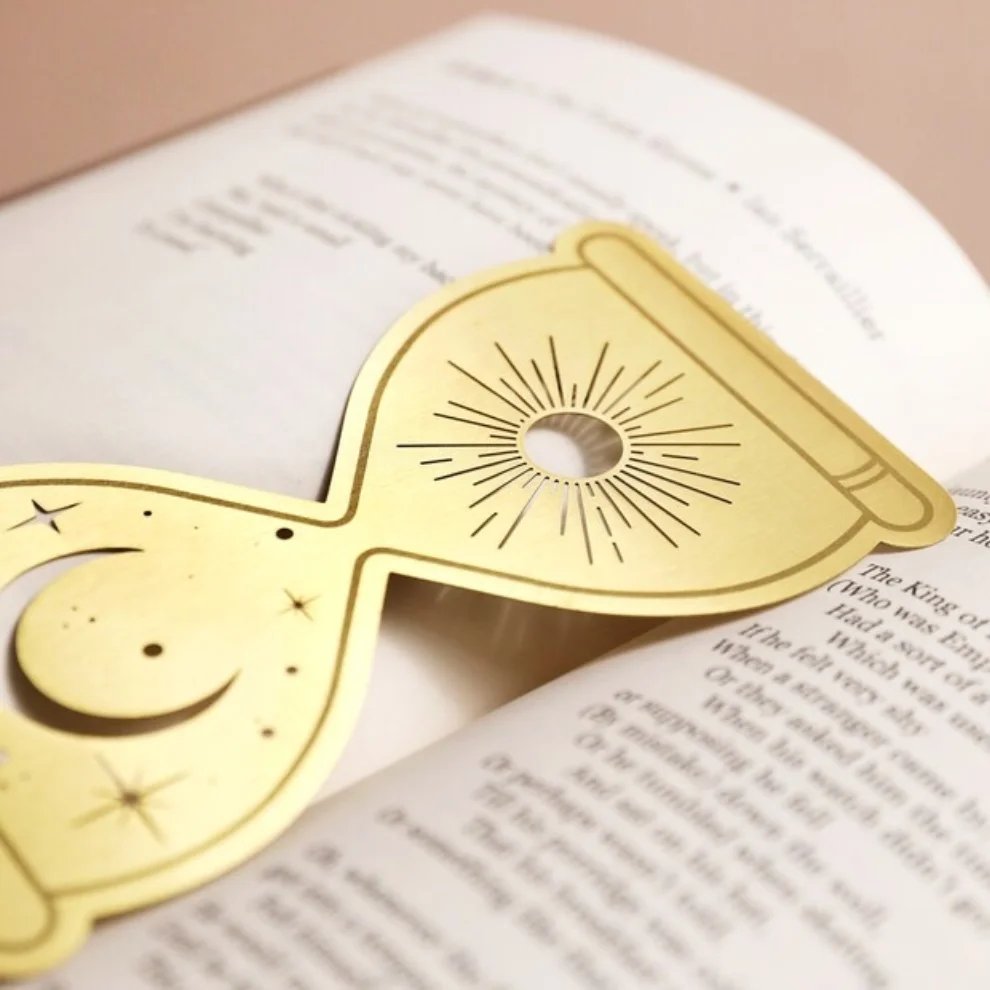 Marcapáginas de metal con diseño astral de luna y sol colocado en un libro antiguo, estilo vintage.