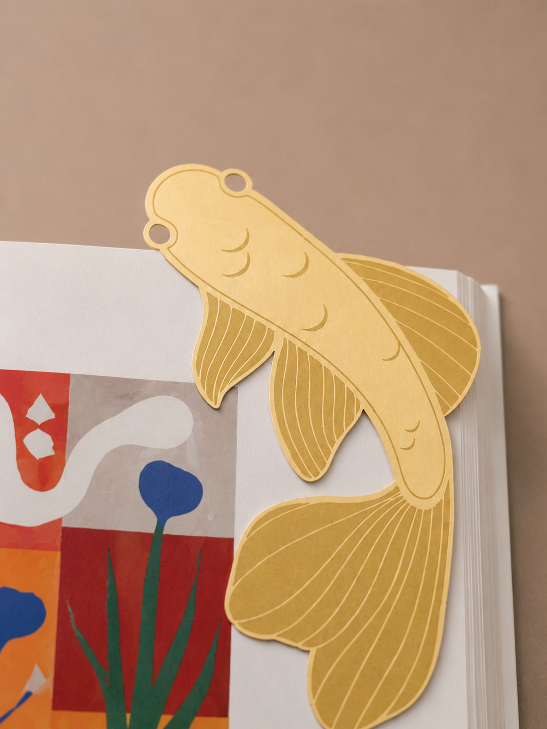 Marcapáginas metálico con forma de pez koi colocado entre las páginas de un libro.