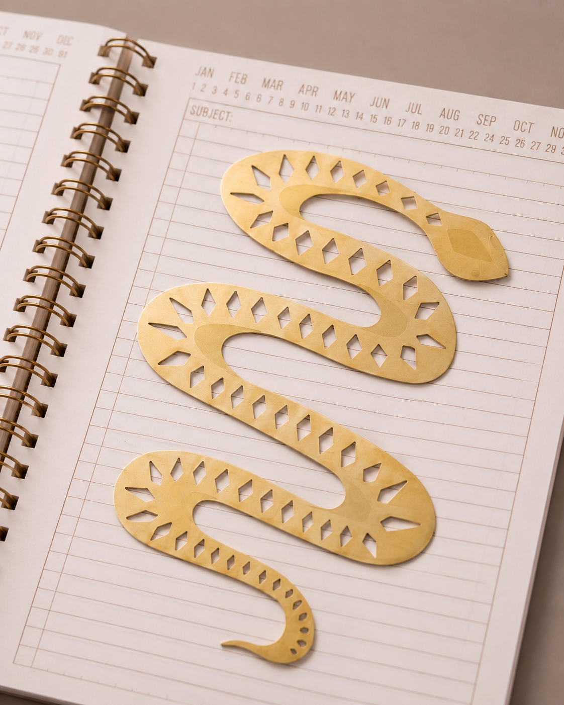 Marcapáginas metálico con forma de serpiente dorada colocado sobre un cuaderno.